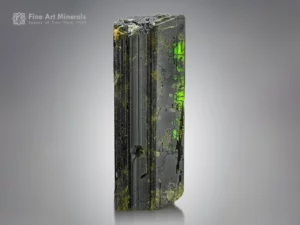 Dark epidote crystal showing bright green flashes when backlit with strong vertical striations.