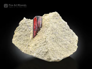 Sharp red brookite crystal emerging from a light earthy matrix