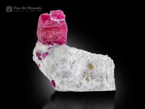 Red ruby crystal on matrix glowing under UV light with strong contrast and fine luster.