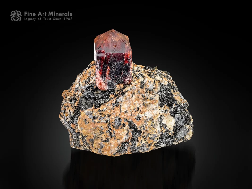 Red zircon crystal with waxy luster perched on matrix in a self-standing display.